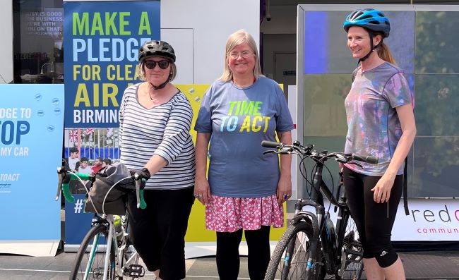 Three people at Clean Air day event at New Street Station. Two of them are wearing cycle helmets and are stood next to their bicycles. All three people are smiling at the camera.