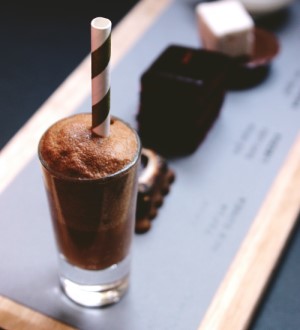 A glass of foaming hot chocolate with a striped, paper straw in the glass.